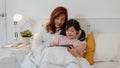 Asian grandmother using tablet read fairy tales to granddaughter at home. Senior Chinese, grandma happy relax with young girl Royalty Free Stock Photo