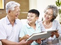 Asian grandparents and grandchild reading a book together Royalty Free Stock Photo