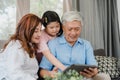 Asian grandparents and granddaughter using tablet at home. Senior Chinese, grandpa and grandma happy spend family time relax with