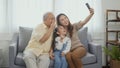 Asian grandparents laughing taking selfie with granddaughter on sofa at home by mobile Royalty Free Stock Photo