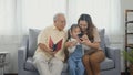 Asian grandparents laughing taking selfie with granddaughter on sofa at home by mobile Royalty Free Stock Photo