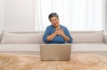 Asian gray hair old woman looking at laptop computer monitor, place both hands on the chest while sit on sofa in the living room Royalty Free Stock Photo