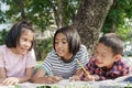 Asian Group elementary school children write a notebook with a pencil and learning together in the summer at park in the morning.