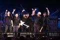Asian group of musician men rock band standing together on stage raising fist and smiling to audience at concert