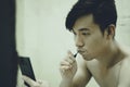 Asian guy brushes his teeth and read the news on smartphone in the bathroom