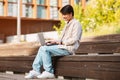 Asian guy sitting on bench at urban area, using laptop Royalty Free Stock Photo