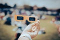 Asian hand wear smart watch holding paper solar eclipse with blurry crowd people watching totality show in Dallas, Texas