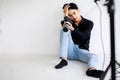 Asian handsome male model wearing casual black shirt with jeans, holding a camera, sitting on white background in a studio and Royalty Free Stock Photo