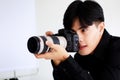Asian handsome male model wearing casual black shirt with jeans, holding a camera, sitting on white background in a studio and Royalty Free Stock Photo