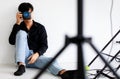 Asian handsome male model wearing casual black shirt with jeans, holding a camera, sitting on white background in a studio and Royalty Free Stock Photo