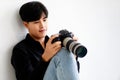 Asian handsome male model wearing casual black shirt with jeans, holding a camera, sitting on white background in a studio and Royalty Free Stock Photo