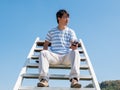 Asian handsome man holding mobile phone, sitting on stair in nature blue sky