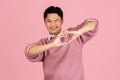 Asian handsome man in sweater standing on isolated pink background. He is smiling in love making a heart symbol with hands. Royalty Free Stock Photo