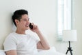 Asian handsome man talk on mobile phone call on bed at home in morning. Happy attractive male lying down in bedroom enjoy holiday Royalty Free Stock Photo