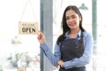 Asian Happy business woman is a waitress in an apron, the owner of the cafe stands at the door with a sign Open waiting Royalty Free Stock Photo