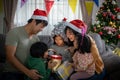 Asian Happy family with daughter in Santa hats gathered together on Christmas time and enjoy gifts box opening