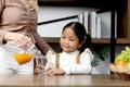 Asian happy family spending time together, mother pouring fresh orange juice from jug for her little cute daughter sitting in Royalty Free Stock Photo