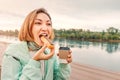 Happy girl eats a fresh French dessert Eclair and drinks coffee. Street food takeaway. Recreation and leisure on the city Royalty Free Stock Photo