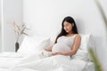 Asian happy pregnant woman is sitting and reading a book on bed and and touching her belly Royalty Free Stock Photo