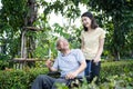 Asian happy Senior retired grandfather enjoy outdoor at green park. Attractive girl daughter pushing elderly father on wheelchair Royalty Free Stock Photo