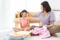 Asian happy smiling mother put her hand on cute daughter head. They are sitting on a floor at home while helping folding clothes Royalty Free Stock Photo