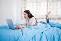 Asian happy young woman wear headphones and listening music song and watching website for shopping online from laptop  on bed at Royalty Free Stock Photo