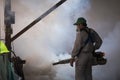 Asian healthcare worker using fogging machine spraying chemical to eliminate mosquitoes and prevent dengue fever in warehouse area