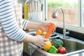 Asian healthy woman washing an carrot and other fvegetable above kitchen sink and cleaning a fruit / vegetable with water to