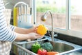 Asian healthy woman washing yellow bell pepper and other vegetable above kitchen sink and cleaning a fruit / vegetable with water Royalty Free Stock Photo