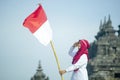 Asian Hijab Holding Indonesian flag with clear blue skyand Plaosan Temple background, Indonesia independence day Royalty Free Stock Photo