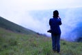 Asian hiking or tourist woman in dark blue sweater with camera standing on green grass field with mountain view and mist Royalty Free Stock Photo