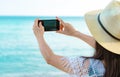 Asian hipster woman wear hat use smartphone taking photo of beautiful sea. Summer vacation at tropical paradise beach. Happy Royalty Free Stock Photo