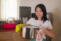 Asian home cook girl lifestyle portrait . Young happy and beautiful Chinese woman in kitchen apron and glove holding cooking pot Royalty Free Stock Photo