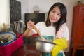 Asian home cook girl lifestyle portrait . Young happy and beautiful Chinese woman in kitchen apron and glove holding cooking pot Royalty Free Stock Photo