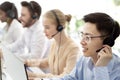 Asian hotline operator and his colleagues working at modern call centre office, copy space Royalty Free Stock Photo