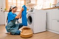 Asian housekeeper or housemaid hold and check blue cloth before put into washing machine during home service to customer Royalty Free Stock Photo