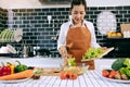 Asian housewife is using tongs to take the salad on the wooden cutting board onto the salad cup in the kitchen room Royalty Free Stock Photo