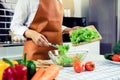 Asian housewife is using tongs to take the salad on the wooden cutting board onto the salad cup in the kitchen room Royalty Free Stock Photo