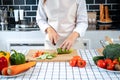 Asian housewife wearing apron and using knife to slice cucumber and tomato on chopping board