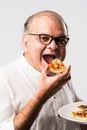 Asian Indian old man eating pizza with funny expressions Royalty Free Stock Photo