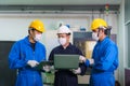 Asian industrial engineers and worker in hard hats discuss product line in laptop and make showing gestures and work in a heavy