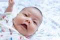 Asian Infant baby is ralaxing on the white bed. It is watching at me. It`s face is frown. Royalty Free Stock Photo