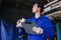 Asian Japanese mechanic male worker employee checking car in auto service workshop maintenance replace fix auto part checklist Royalty Free Stock Photo