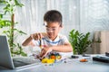 Asian kid boy assembling the Arduino robot car homework project at home