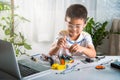 Asian kid boy assembling the Arduino robot car homework project at home
