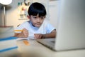 Asian Kid Boy Focused on Homework and Learning Online Alone with Laptop in Room at Home, Concentrating on Learning and Doing Royalty Free Stock Photo