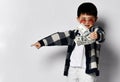 Asian kid boy in sunglasses, plaid cardigan and white pants shows bunch fan of dollars cash money and points to the side