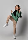 Asian kid girl in green earmuffs, sportswear and white sneakers stands on one leg holding knee up and gesturing, dancing Royalty Free Stock Photo
