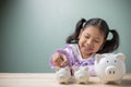 An Asian kid girl put a coin in a white pig piggy bank on a wood table at home. Save money for tuition fees, the cost of school Royalty Free Stock Photo