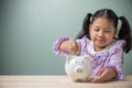 An Asian kid girl put a coin in a white pig piggy bank on a wood table at home. Save money for tuition fees, the cost of school Royalty Free Stock Photo